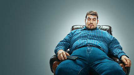 Image showing Fat man sitting in a brown armchair, emotional watching TV