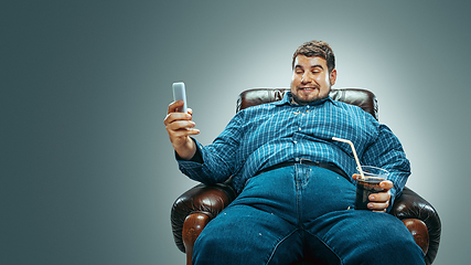 Image showing Fat man sitting in a brown armchair, emotional watching TV