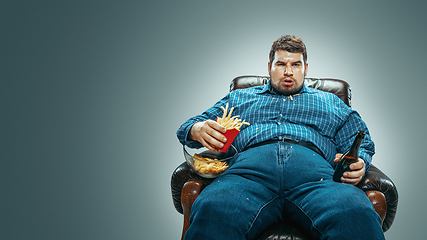 Image showing Fat man sitting in a brown armchair, emotional watching TV