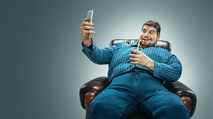 Image showing Fat man sitting in a brown armchair, emotional watching TV