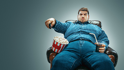 Image showing Fat man sitting in a brown armchair, emotional watching TV