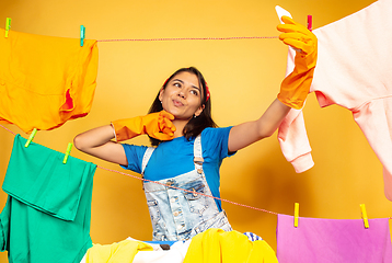 Image showing Funny and beautiful housewife doing housework on yellow background