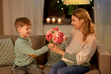 Image showing smiling little son gives flowers to mother at home