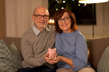 Image showing happy senior couple with piggy bank at home