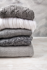 Image showing Stack of cozy knitted sweaters and pullovers on wooden background. 