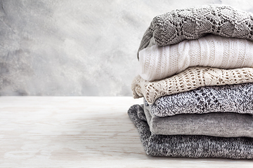 Image showing Stack of cozy knitted sweaters and pullovers on wooden background. 