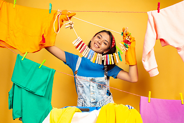 Image showing Funny and beautiful housewife doing housework on yellow background