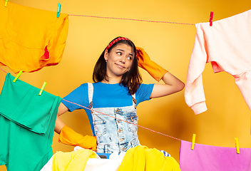 Image showing Funny and beautiful housewife doing housework on yellow background