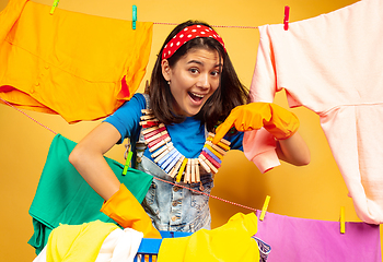 Image showing Funny and beautiful housewife doing housework on yellow background