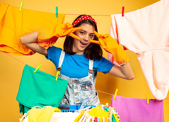 Image showing Funny and beautiful housewife doing housework on yellow background