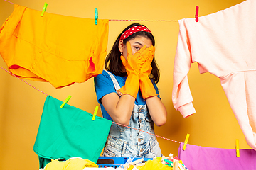 Image showing Funny and beautiful housewife doing housework on yellow background