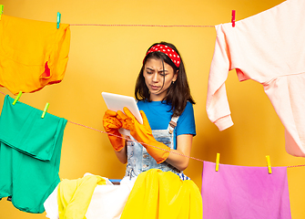 Image showing Funny and beautiful housewife doing housework on yellow background