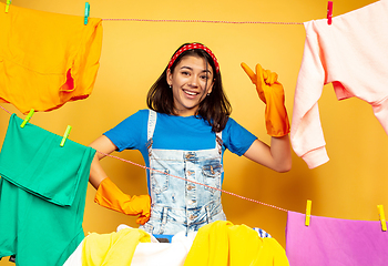 Image showing Funny and beautiful housewife doing housework on yellow background