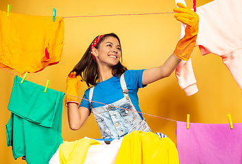 Image showing Funny and beautiful housewife doing housework on yellow background