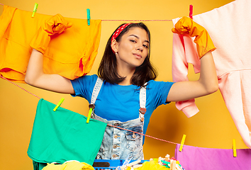 Image showing Funny and beautiful housewife doing housework on yellow background
