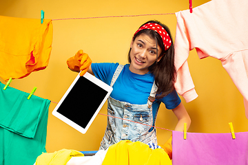 Image showing Funny and beautiful housewife doing housework on yellow background