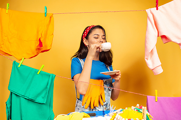 Image showing Funny and beautiful housewife doing housework on yellow background