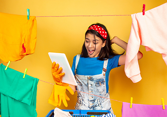 Image showing Funny and beautiful housewife doing housework on yellow background