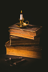 Image showing Pile of old antique books with candle in vintage style on black background