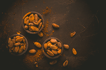 Image showing Organic cocoa beans in small bowls on brown background