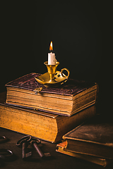 Image showing Pile of old antique books with candle in vintage style on black background