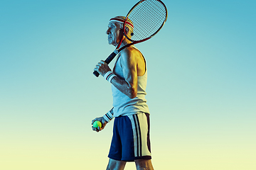 Image showing Senior man playing tennis in sportwear on gradient background and neon light