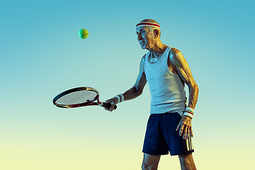 Image showing Senior man playing tennis in sportwear on gradient background and neon light