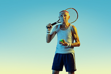 Image showing Senior man playing tennis in sportwear on gradient background and neon light