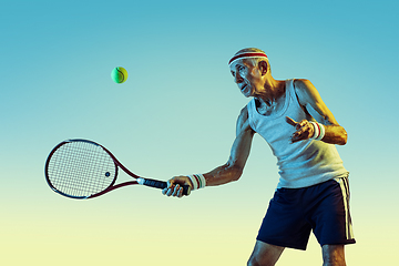 Image showing Senior man playing tennis in sportwear on gradient background and neon light