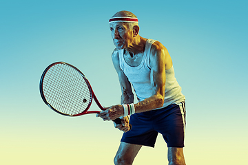 Image showing Senior man playing tennis in sportwear on gradient background and neon light