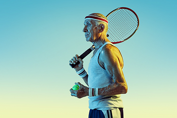 Image showing Senior man playing tennis in sportwear on gradient background and neon light