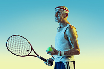 Image showing Senior man playing tennis in sportwear on gradient background and neon light