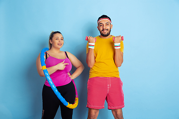 Image showing Young pretty caucasian couple in bright clothes training on blue background