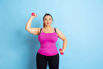 Image showing Young caucasian plus size female model\'s training on blue background