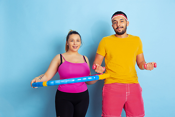 Image showing Young pretty caucasian couple in bright clothes training on blue background