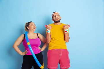 Image showing Young pretty caucasian couple in bright clothes training on blue background