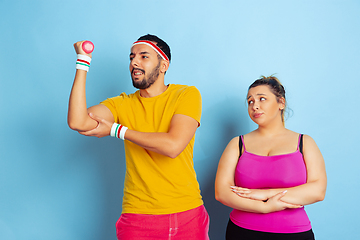 Image showing Young pretty caucasian couple in bright clothes training on blue background