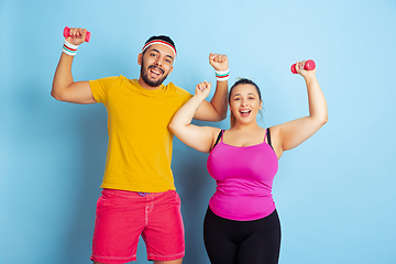 Image showing Young pretty caucasian couple in bright clothes training on blue background