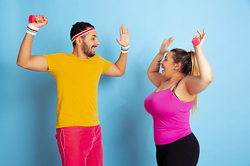 Image showing Young pretty caucasian couple in bright clothes training on blue background