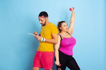 Image showing Young pretty caucasian couple in bright clothes training on blue background