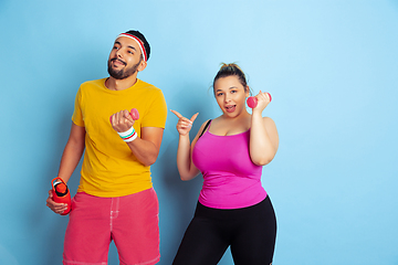 Image showing Young pretty caucasian couple in bright clothes training on blue background
