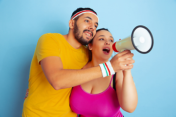 Image showing Young pretty caucasian couple in bright clothes training on blue background