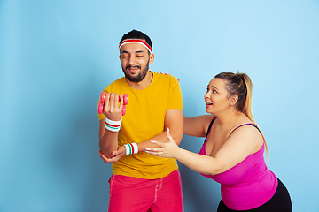 Image showing Young pretty caucasian couple in bright clothes training on blue background