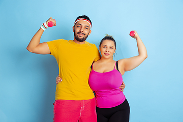 Image showing Young pretty caucasian couple in bright clothes training on blue background