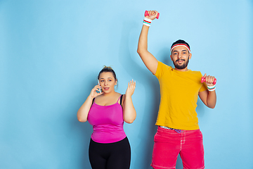 Image showing Young pretty caucasian couple in bright clothes training on blue background