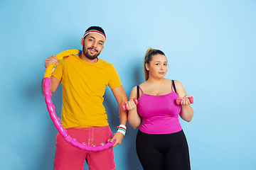 Image showing Young pretty caucasian couple in bright clothes training on blue background