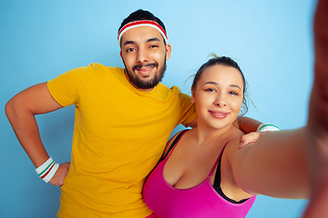 Image showing Young pretty caucasian couple in bright clothes training on blue background