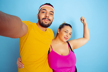 Image showing Young pretty caucasian couple in bright clothes training on blue background