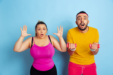 Image showing Young pretty caucasian couple in bright clothes training on blue background