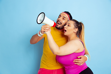 Image showing Young pretty caucasian couple in bright clothes training on blue background